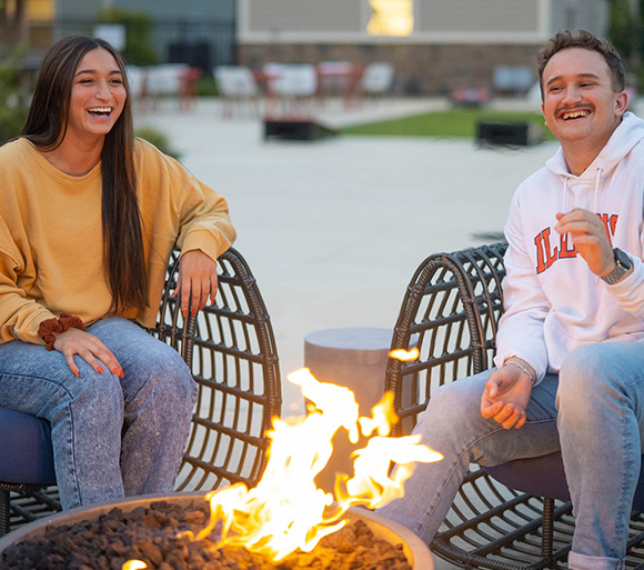 A woman and a man sitting by a campfire.